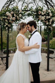 a bride and groom are standing under an arch with flowers on it at the end of their wedding day