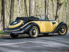 an old yellow and black car parked on the side of the road in front of some trees