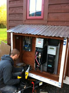 a man working on an electrical device in the back of a truck parked next to a house