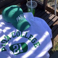 a baseball cap, sweatshirt and drink sitting on a bench