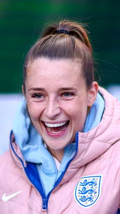 a smiling woman in a pink jacket with a blue and white emblem on it's chest