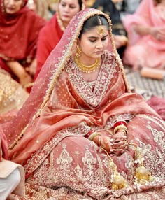 a woman in a red and gold bridal gown sitting on the ground with other people