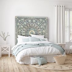 a bedroom with white walls and wood flooring has a large headboard over the bed