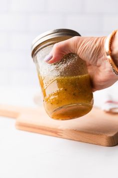 a person holding a jar filled with food on top of a cutting board next to a knife