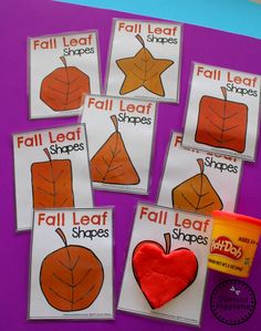 four fall leaf shapes are shown on a purple surface with an orange cup and two red apples