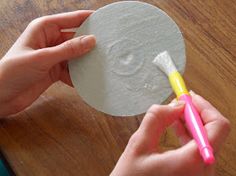 a person is holding a small piece of paper with a toothbrush in it while another hand holds a yellow and pink pen