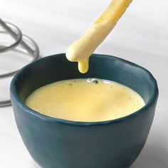 a piece of bread sticks sticking out of a bowl of liquid in front of a computer mouse