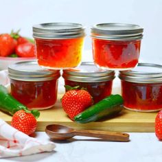 several jars of jam with strawberries and cucumbers next to them on a cutting board