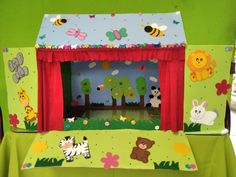 a green table topped with a puppet house and stuffed animals on it's sides