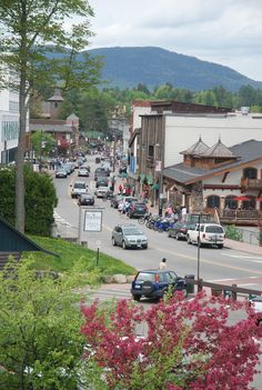 cars are driving down the street in front of buildings and trees with mountains in the background