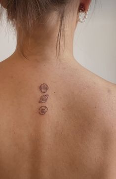 the back of a woman's neck with tattoos on it and seashells