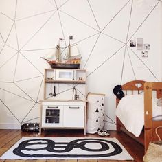 a room with a bed, dresser and toy ship on top of the shelf next to it