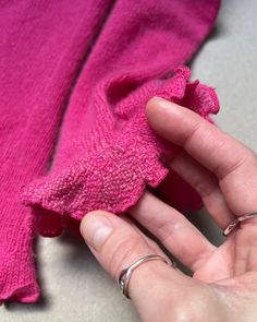 a person is holding something in their hand while wearing a pink sweater with ruffles on it