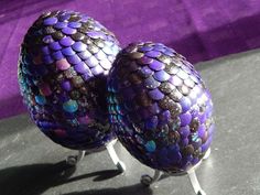 two purple and blue mosaic eggs sitting on top of each other in front of a purple background