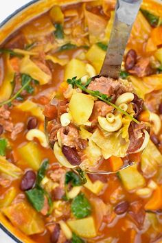 a spoon full of soup with pasta, beans and spinach in it is being lifted from the pot