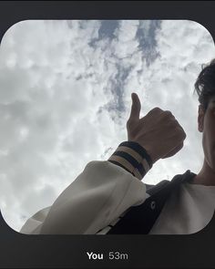 a man with his thumb up in front of the sky and clouds above him, making a thumbs up sign