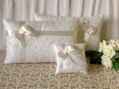 two white pillows with bows on them sitting on a bed next to flowers and a vase