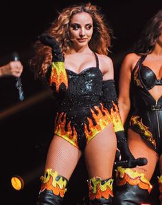 two beautiful women dressed in black and yellow outfits with flames all over them on stage