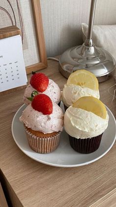 three cupcakes on a plate with lemon slices and strawberries next to each other