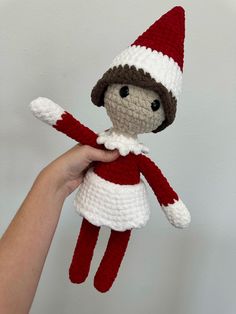 a hand holding a crocheted doll with a red and white hat on it's head