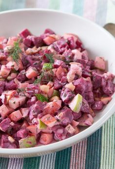 a white bowl filled with beet salad on top of a striped table cloth next to a wooden spoon