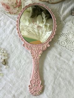 a pink mirror sitting on top of a table next to some doily and flowers