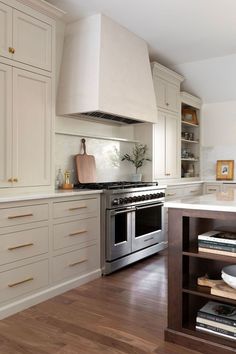 a kitchen with white cabinets and stainless steel stove top oven in the center, surrounded by wooden flooring