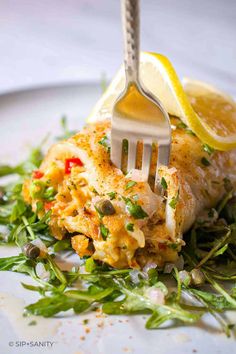 a fork is stuck into some food on a plate with lemon wedges and greens