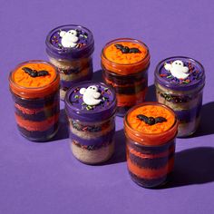 four jars filled with halloween treats sitting on top of a purple surface