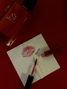 a bottle of perfume next to a piece of paper with lipstick on it