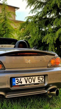 the back end of a silver car parked on top of green grass next to trees