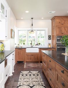 a large kitchen with wooden cabinets and black counter tops, along with a rug on the floor