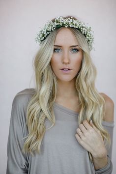 a woman with long blonde hair wearing a white flower crown on her head and gray shirt