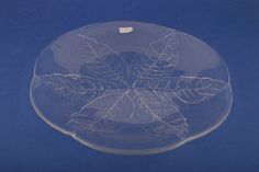 a clear glass plate with leaves etched on the front and sides, sitting on a blue surface