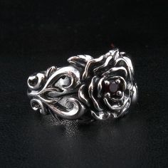 As if plucked from an English garden, our Rose Ring is a piece of true craftsmanship. An exquisite accessory for the man or women seeking unique style, it celebrates everything there is to adore about these exquisite blooms. As the petals unfurl, they reveal a dark garnet stone nestled within. And the intricate detail extends effortlessly around the band to create beauty at every angle.  This piece has been carefully crafted by the hands. It has a solid sterling silver construction, affording it Elegant Promise Ring With Rose Design, Elegant Adjustable Rose-colored Ring, Rose Design Promise Jewelry, Elegant Silver Rings With Rose Details, Elegant Sterling Silver Rose Design Flower Ring, Elegant Sterling Silver Rings With Roses, Vintage Rose Flower Ring With Rose Design, Elegant Adjustable Flower Ring With Roses, Flower Shaped Rose Ring For Anniversary