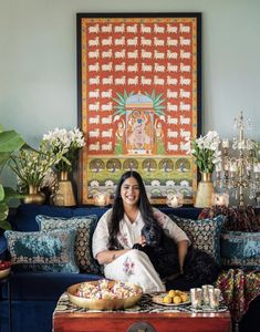 a woman sitting on top of a blue couch next to a table filled with food