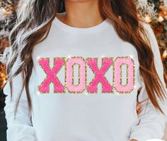 a woman wearing a white shirt with the word xoxo in pink sequins