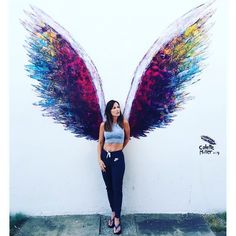 a woman leaning against a wall with wings painted on it