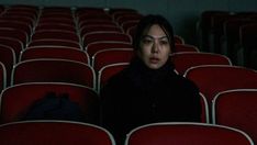 a woman sitting in the middle of a row of red chairs with her eyes closed