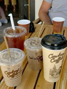 three cups of coffee sitting on top of a wooden table with straws in them