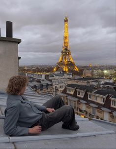 a man sitting on the roof of a building in front of the eiffel tower