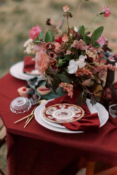 a red table cloth topped with plates and flowers