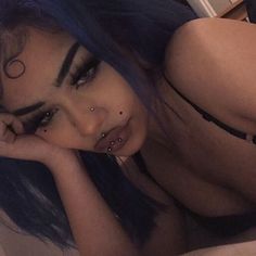 a woman with blue hair and piercings laying on a bed looking at the camera