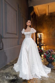 a woman in a white wedding dress standing by a building with her hands on her hips