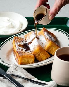 powdered sugar being drizzled onto french toast on a plate with coffee