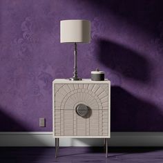 a white cabinet sitting in front of a purple wall with a lamp on top of it