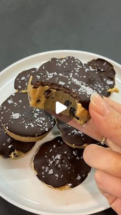 a person is taking a bite out of chocolate covered doughnuts on a plate