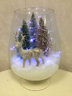 a glass bowl filled with snow covered trees and a reindeer figurine in the center