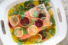 fish with lemons, herbs and spices in a white dish on top of a table