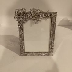 an ornate silver frame with crystal flowers on the top and bottom, sitting on a white surface